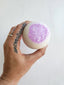 Hand holding a bath bomb with purple glitter on a light background