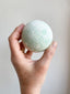Hand holding a green bath bomb against a plain background