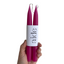 Two pink candles held by a hand with a white label displaying 'aide' on a white background