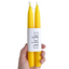 Yellow candles with a white label displaying 'aide' held by a hand against a white background