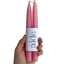 Pink candles with a white label displaying the word 'aide' held by a hand on a white background