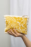 Hand holding a yellow floral-patterned pouch against a plain background