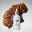 White bottle with a dropper labeled 'Rainbow Reishi' on a gray background with a large piece of reishi mushroom.