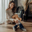 Woman sitting on the floor wearing a beige sweater and patterned socks in a cozy room.