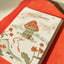 Greeting card with a frog illustration and 'New Home!' text on a red surface