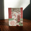 A square greeting card with a vintage-style illustration of a table scene, featuring red curtains, coffee cups, and a French press, with the text 'so HAPPY to spend my DAYS with YOU!' on the front, standing on a wooden table.