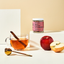 Jar of 'Apple Crumble Ashwagandha' supplement with a cup of tea, apples, and cinnamon sticks on a light background