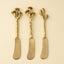 Three gold-handled butter knives with unique designs on a beige background