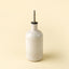 White ceramic oil bottle with a metallic nozzle on a beige background