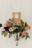 Floral arrangement in a silver vase with a Caramelo's coffee bag on a white wooden background