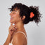 Woman with styled hair using a red hair clip against a light background