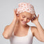 Woman wearing a pink shower cap with cherry pattern on a plain background