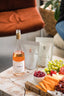 Bottle of rosé wine, cheese platter with fruits and crackers on a wooden table.