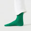 Green sock worn with white pants on a light gray background