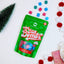 Green package of 'Happy Hippo' mini bath bombs on a snowy background with colorful bath bombs and Christmas decorations.
