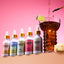 Shroom Soda dropper bottles with a cocktail being poured into a glass on a pink background