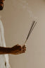Person holding incense sticks with smoke against a neutral background