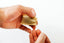 A close-up of a person's hands holding a small beige fabric pouch and pulling a thin white thread through it, against a plain white background.