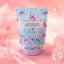 A stand-up pouch of Botanical Propaganda Mini Bombs bath bombs in the 'butterfly garden' scent, featuring pastel purple and green cubes visible through a clear window, set against a pink background with decorative bubbles.