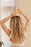 Woman with wavy hair using a yellow hair product in a bright room.