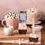 Hot chocolate bomb with marshmallows on a wooden surface with mugs and a package in the background.