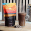 GNAW Hot Chocolate Flakes packaging with a glass of hot chocolate on a wooden surface.