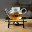Glass teapot with tea on a black stand with a candle, on a wooden surface.