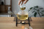 Glass teapot with tea being poured into a glass cup on a wooden table.