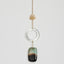 Suncatcher with a clear circular pendant and a green and black rectangular pendant on a light gray background