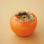 A single ripe orange persimmon with a green-brown calyx, photographed on a warm beige background.