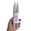 Two beige candles held by a hand with a 'aide' label on a white background