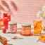 Two jars of 'Lake & Oak' iced tea with strawberry sencha lemonade and ginger peach glow, accompanied by a pink iced tea and peach slices on a pink patterned background.