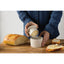 Person spreading butter on bread using a small container on a wooden cutting board.