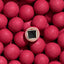 A close-up pile of bright pink round candies, with one cut in half to show a dark chocolate center and white outer layers.