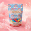 A stand-up pouch of BP Botanicals Mini Bombs candy in 'rainbow power' strawberry cotton candy, styled on a pink background with decorative bubbles.