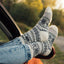 Person wearing patterned socks and jeans sitting in a car with a blurred natural background