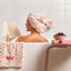 Woman in a bathtub with cherry-themed products, including a towel and book.
