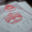 A close-up of a textured white paper print featuring red and gray abstract graphic designs, photographed with a shallow depth of field.