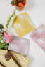 Three skincare packets labeled 'Happy Belly', 'Chill Mama', and 'Glow Mama' on a white surface with flowers and a basket.