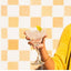 Hand holding a cocktail glass with a lime wedge against a yellow and white checkered background