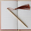 Gold pen with a brown tassel on an open notebook