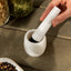 White mortar and pestle on a wooden surface with jars of spices in the background