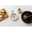 Table setting with ceramic plates, wooden spoon, and small cups on a white marble surface.