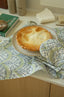 Pie on a plate with a patterned cloth and oven mitt in the foreground
