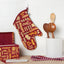 Oven mitt with pasta pattern hanging on a hook next to wooden spoons and a box.