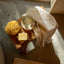 Wooden tray with a yellow sponge, glass jar, and bar of soap on a marble surface.