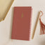 Red notebook with a gold emblem and decorative pen on a light surface