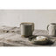 Ceramic mug, bowl with a donut, and teapot on a wooden surface with a neutral background