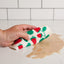 Hand using a strawberry-patterned kitchen towel to clean up a spill on a tiled surface.