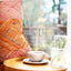 Cup of coffee on a saucer with a decorative hanging light and textured fabric in the background.